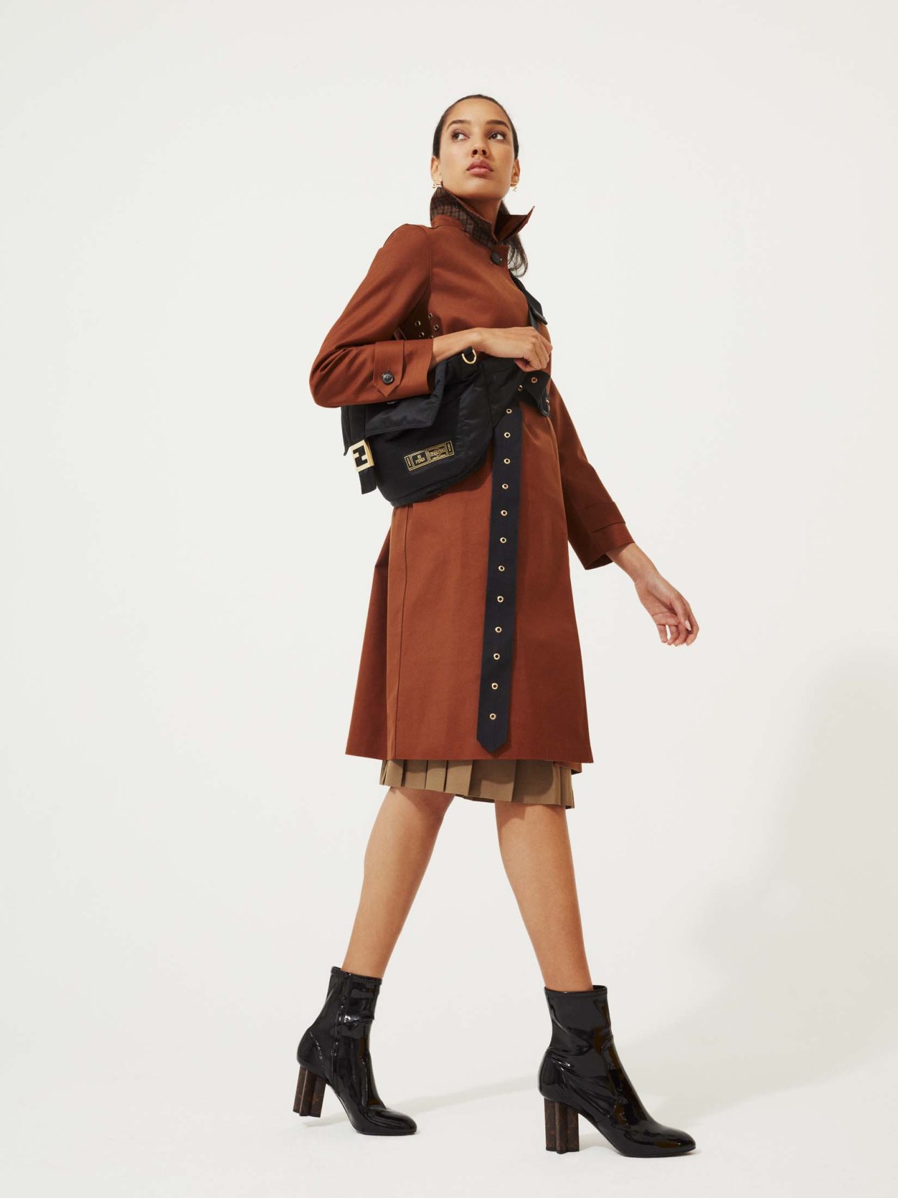 Woman wearing beige trench coat and navy skirt with brown boots and structured handbag