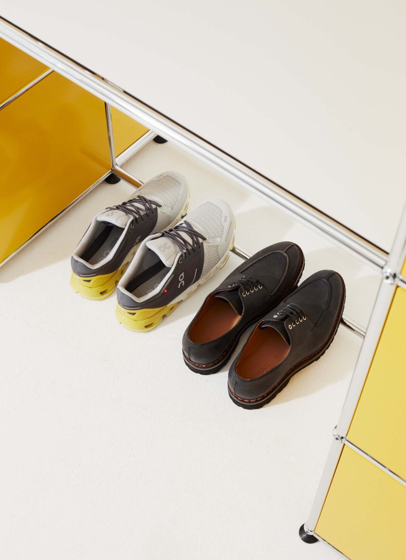 Close-up of white and black On trainers with yellow soles next to brown Heschung leather dress shoes.