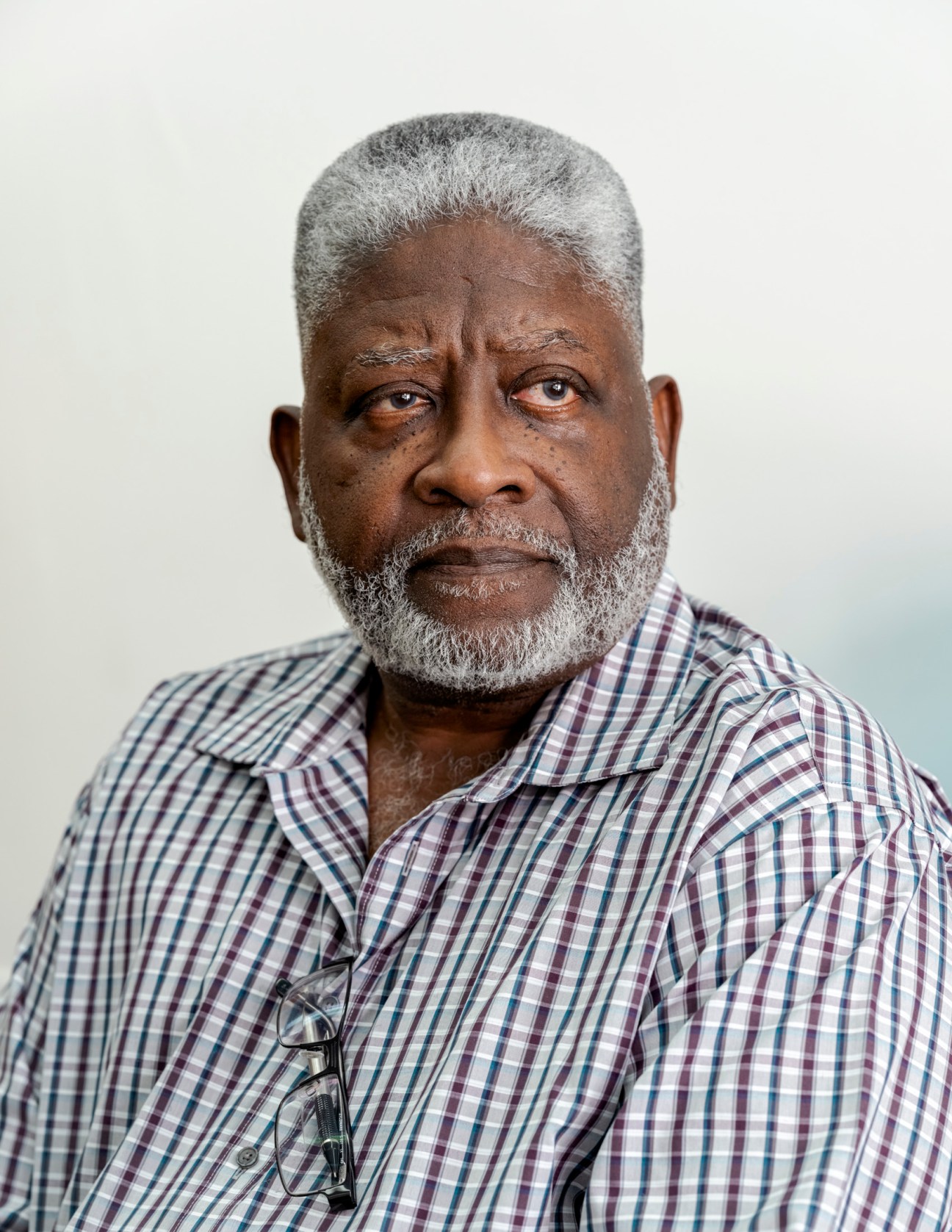 Older man with gray hair and beard wearing a checkered shirt in purple and blue tones.