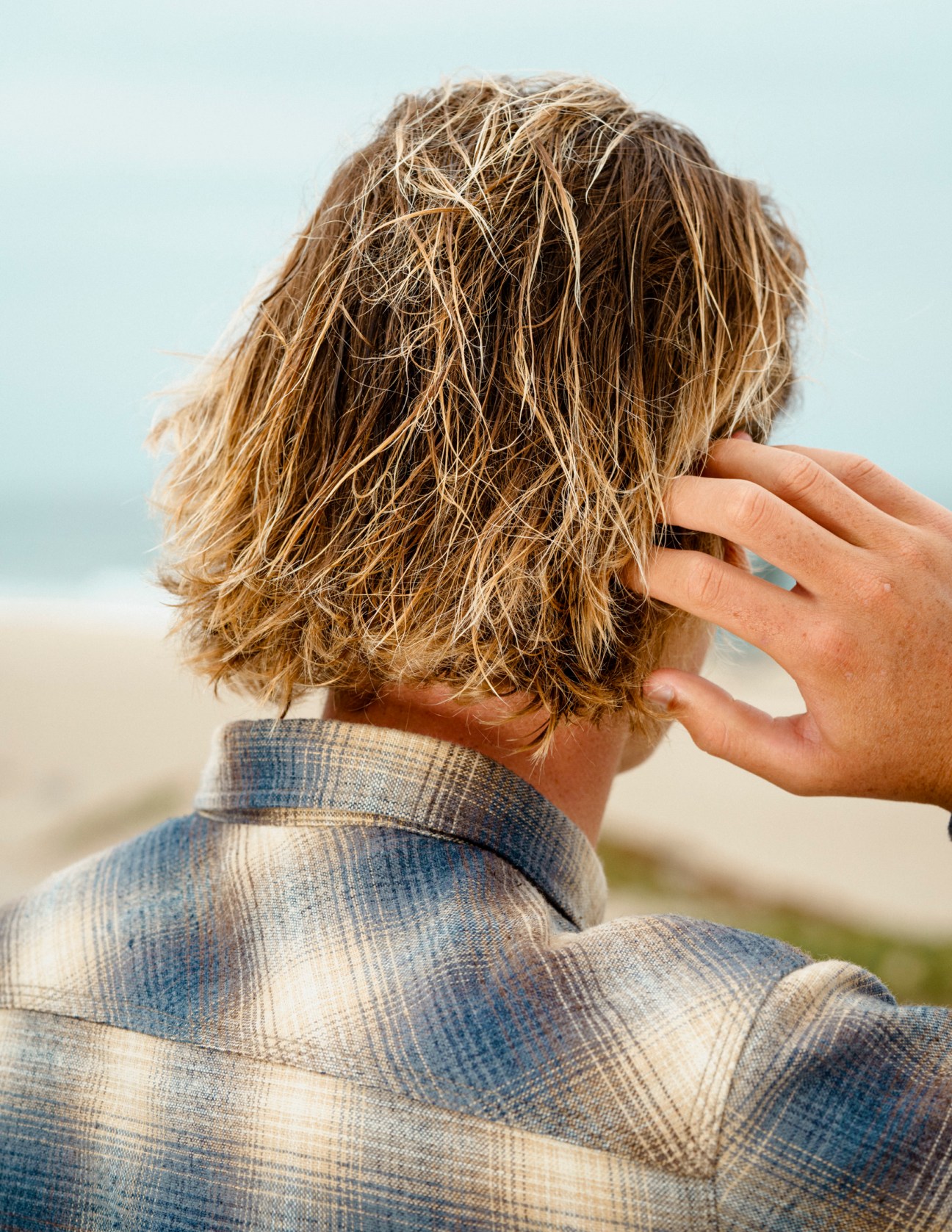 Person shown from behind displaying sun-lightened shoulder-length hair with natural highlights at a beach location.