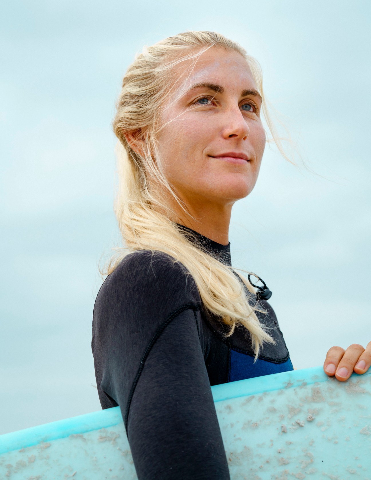Dani, a Lufthansa flight attendant, poses with blonde hair down and a surfboard.