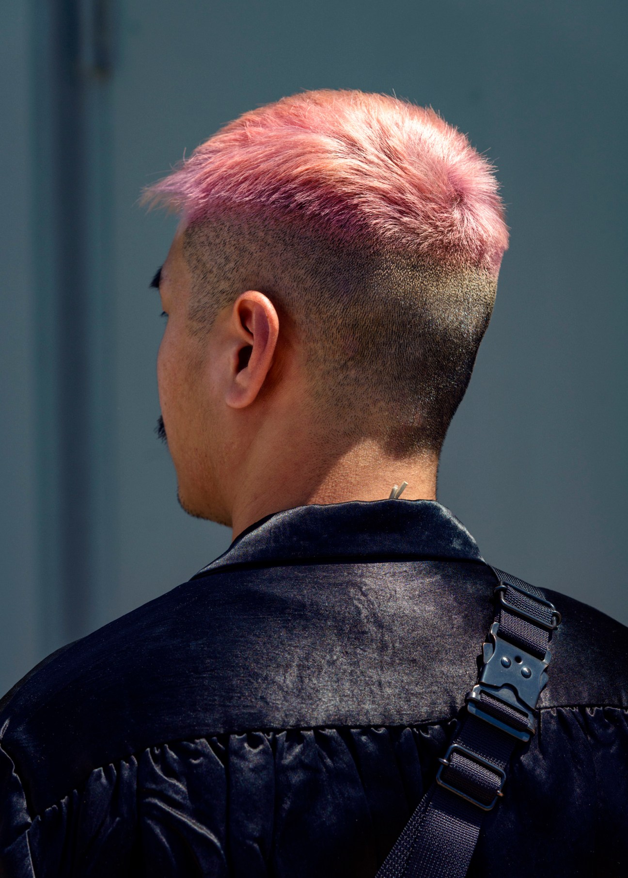 Back view of a person with pink-dyed hair on top and closely shaved sides wearing a black jacket.