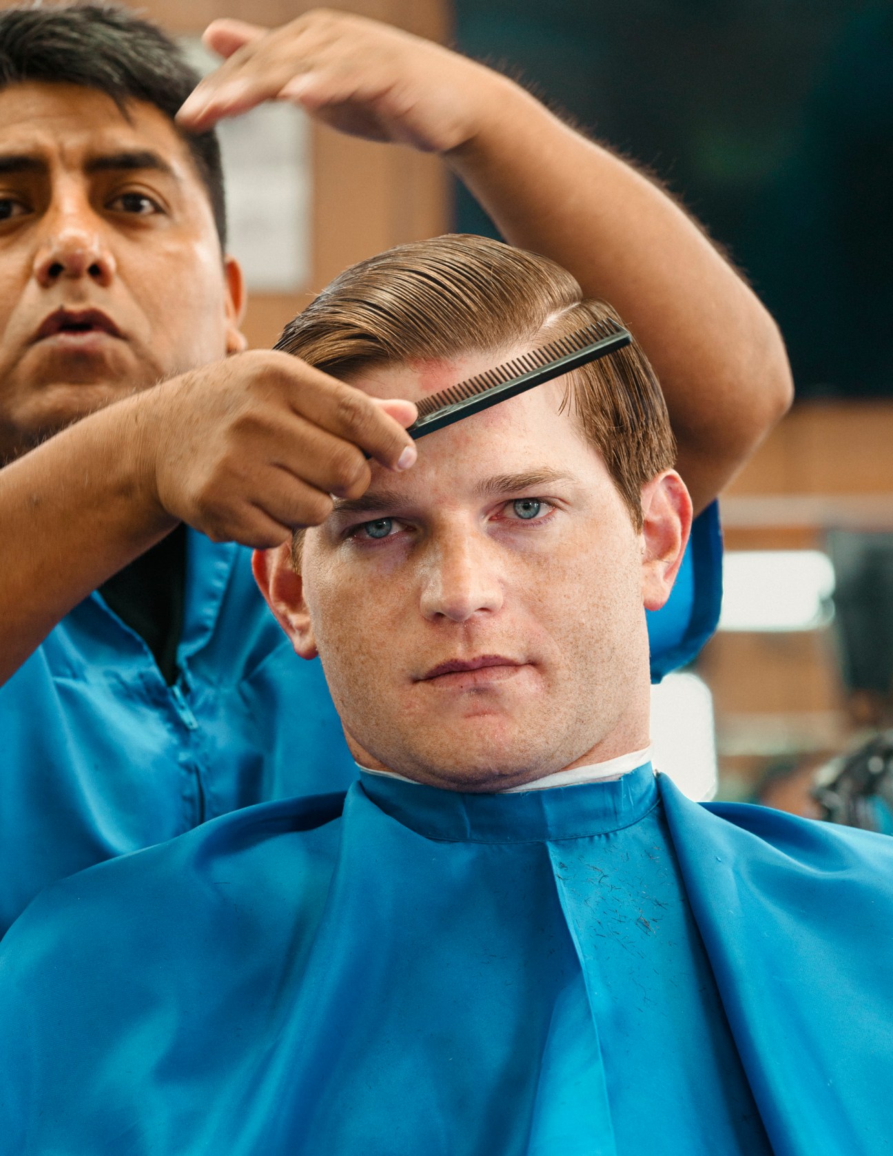 Barber using comb and clippers to cut a customer's hair in a salon.
