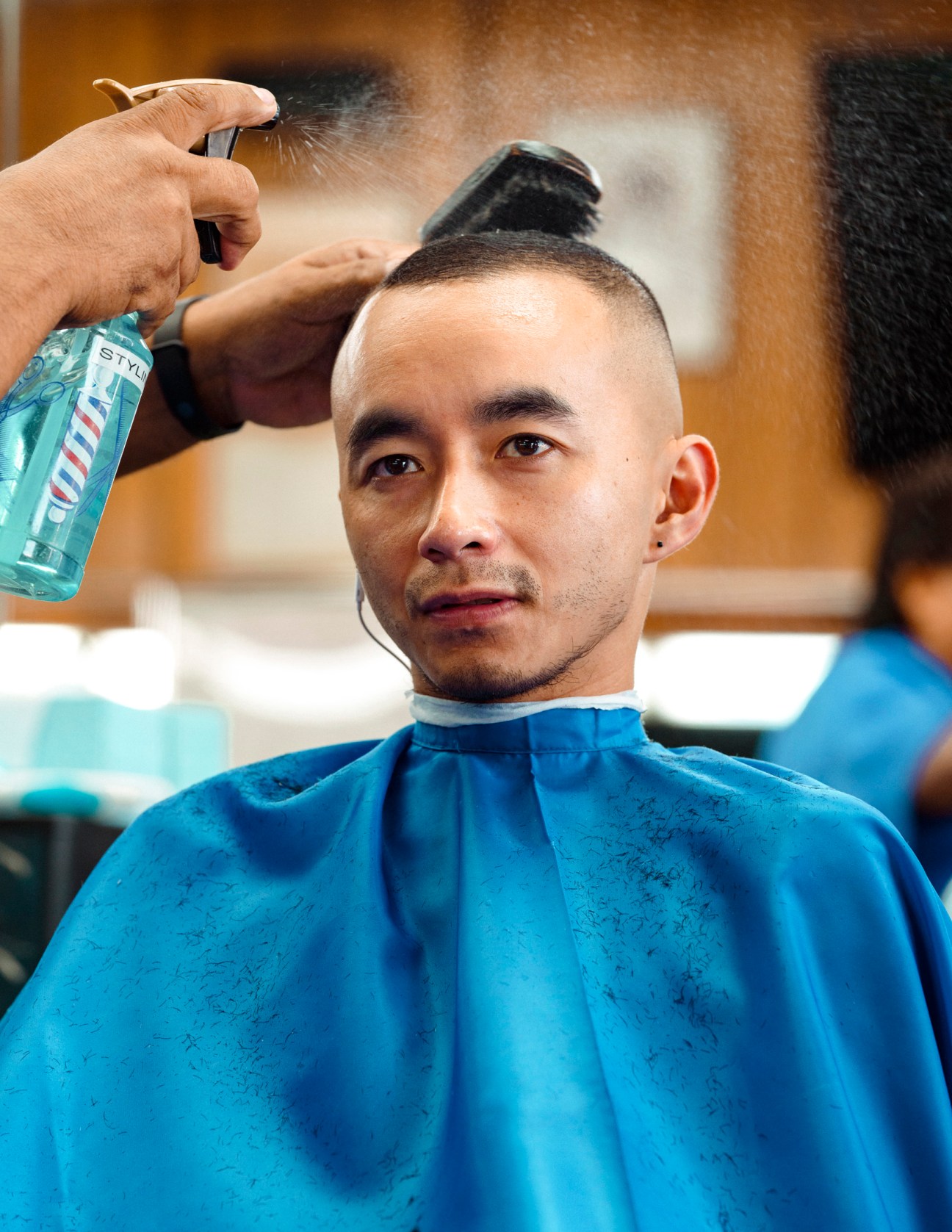 Barber applying styling product to man's short hair with fade and volume on top