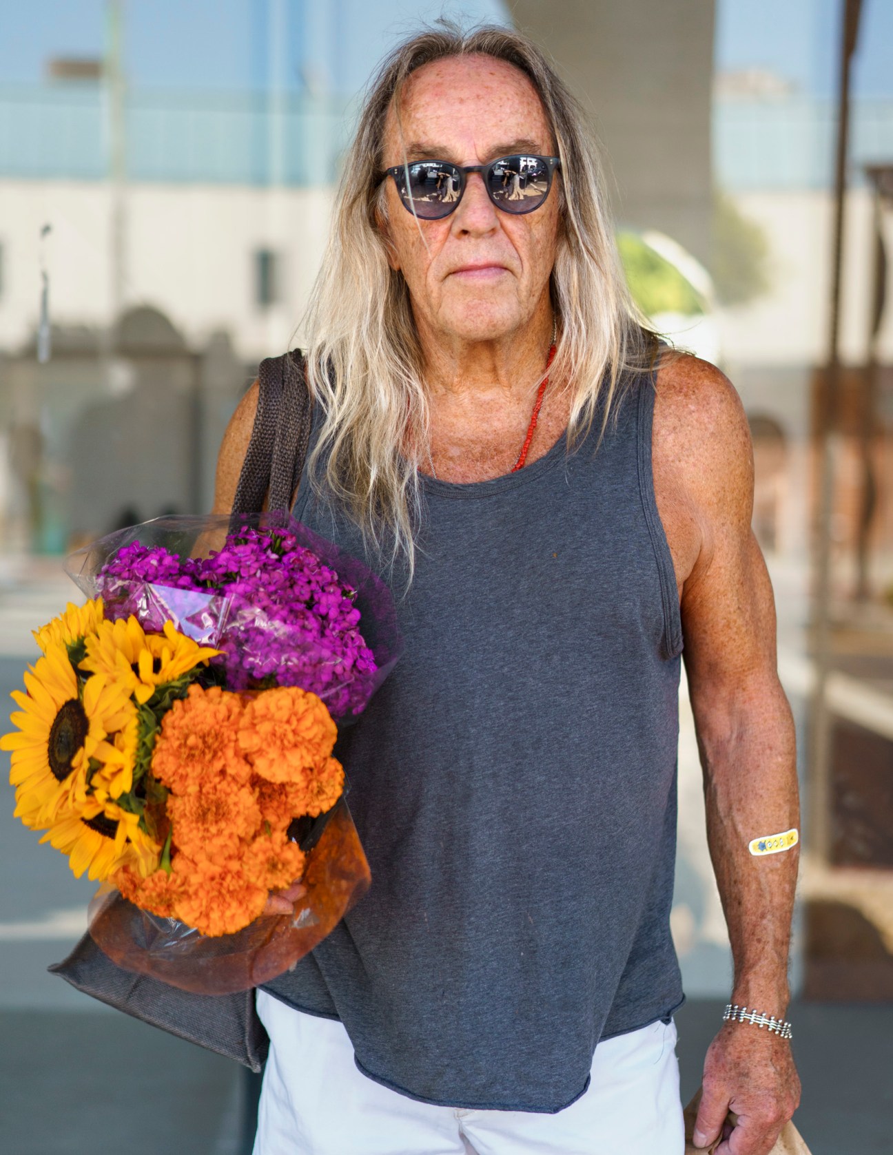 Man with long grey hair wearing sunglasses and holding a bouquet of colorful flowers.