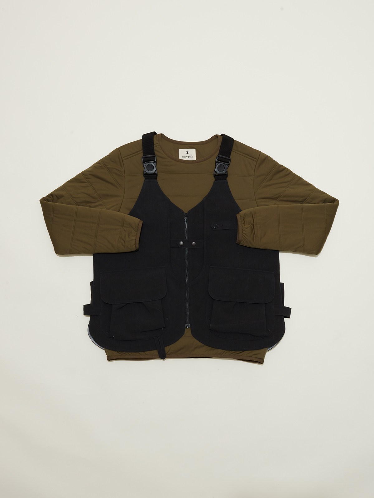 Olive green long-sleeved pullover layered under black multi-pocket vest with adjustable straps