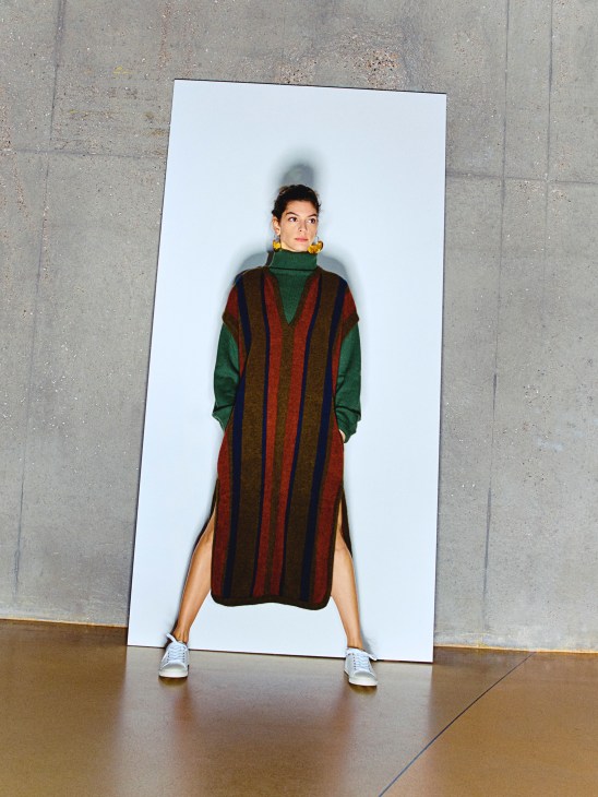 Model wearing a colorful striped dress with green rollneck jumper, white trainers and gold earrings.