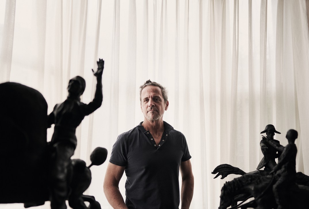 Philipp Humm standing among dark sculptural figures in his London studio space
