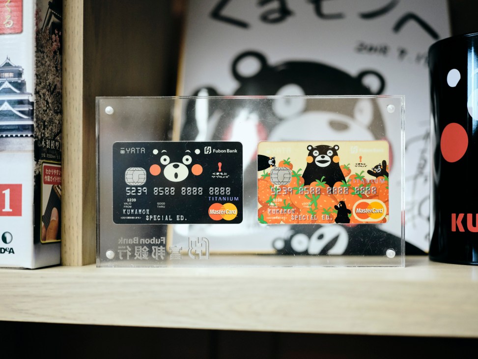Two Kumamon-themed credit cards displayed in a clear acrylic stand on a wooden shelf