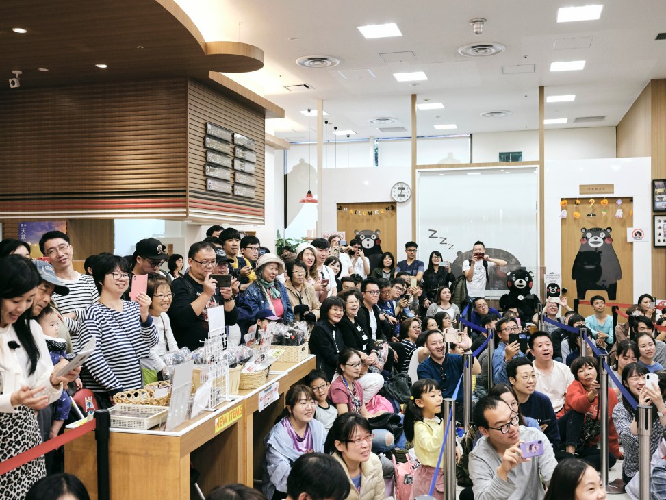 A crowd of enthusiastic fans, many holding cameras and phones, gathered in Kumamon Square waiting to meet their beloved mascot