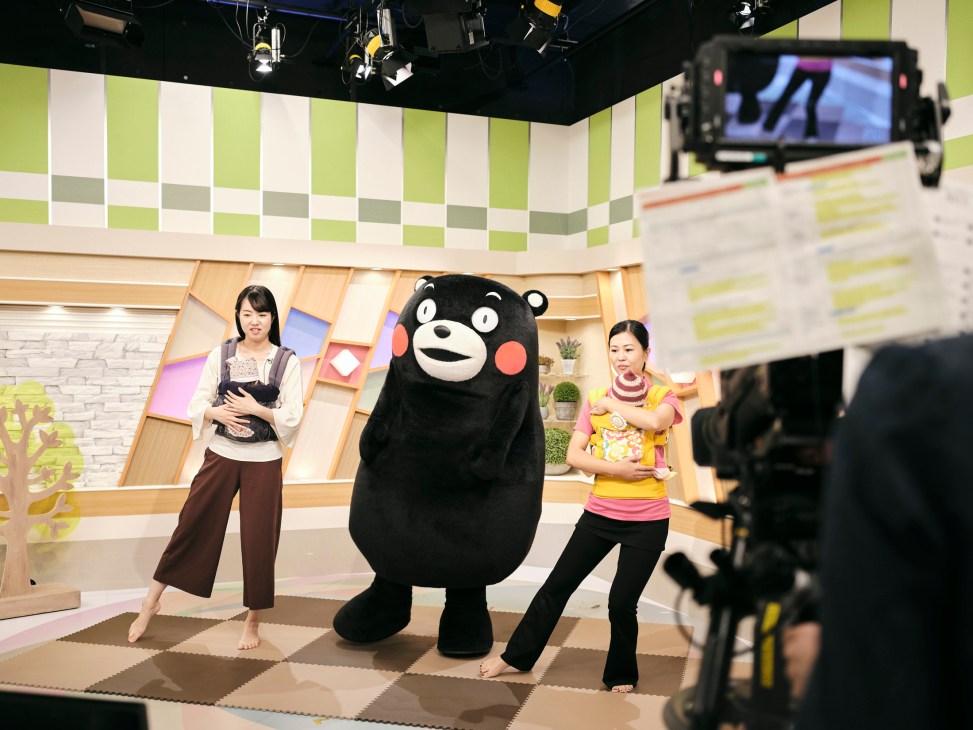 Kumamon mascot with two TV hosts filming at NHK television studio with cameras and professional lighting equipment