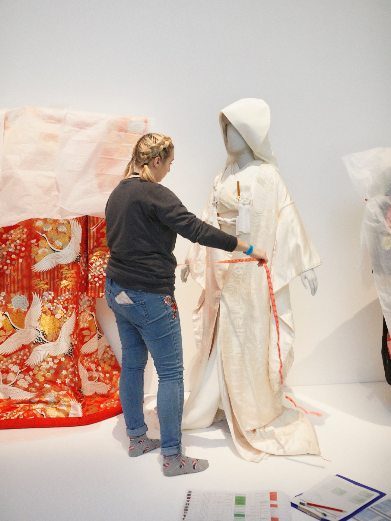 Museum technician measuring a white bridal kimono with measuring tape during exhibition installation