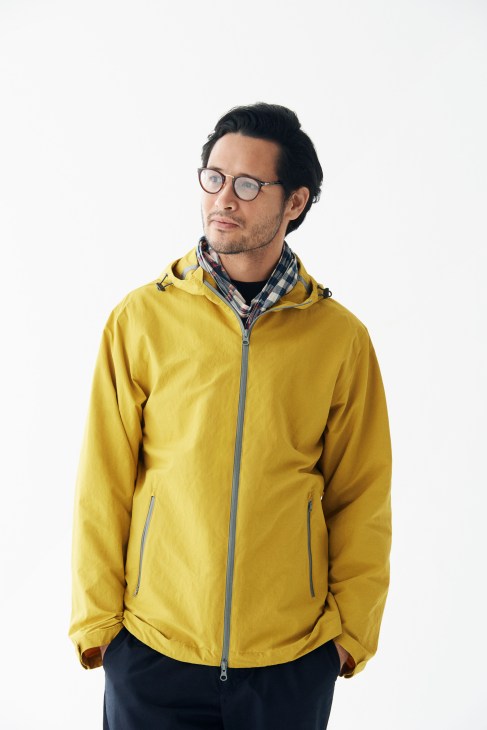 Man wearing yellow Herno jacket with checkered scarf and Persol glasses against white background.