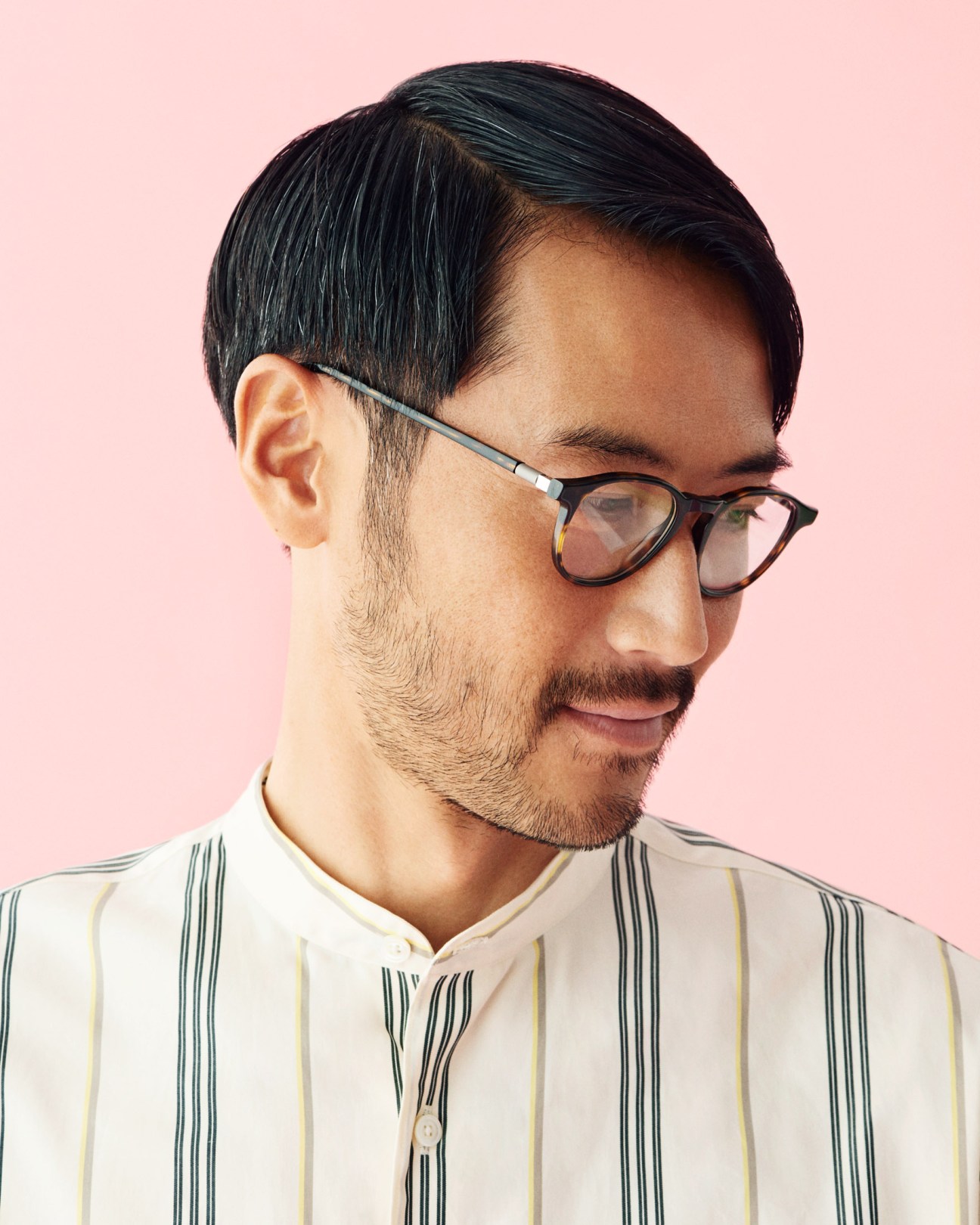 Man wearing tortoiseshell glasses and a striped shirt by Wellder against a pink background.