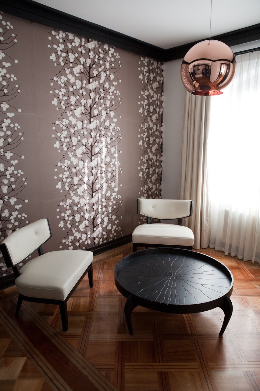 Modern hotel interior with floral wallpaper, white chairs, black table, and copper pendant light.