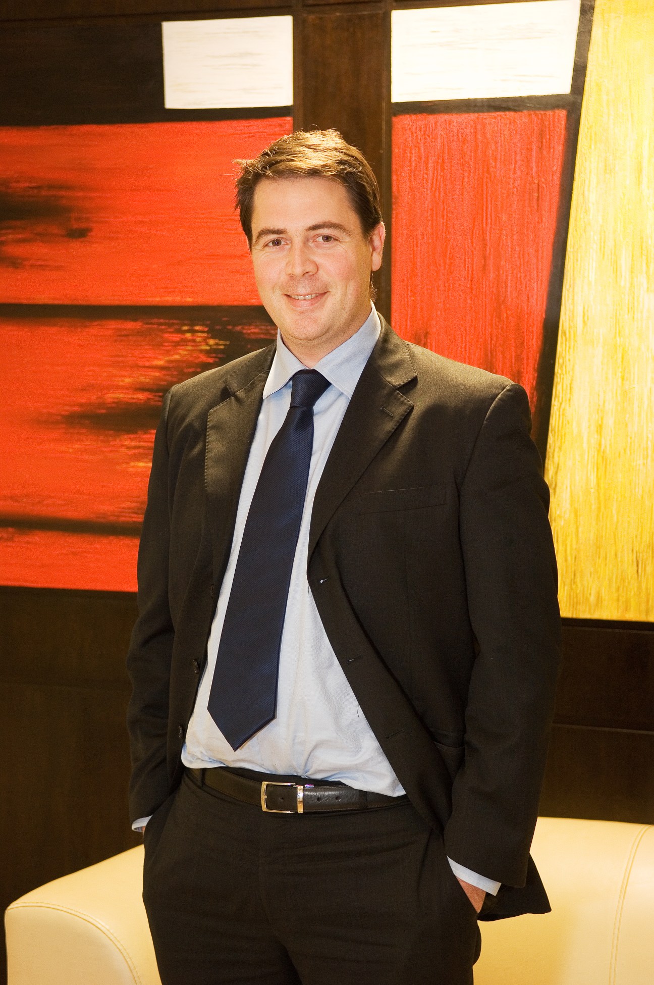 Man in business suit and tie standing against colorful abstract artwork.