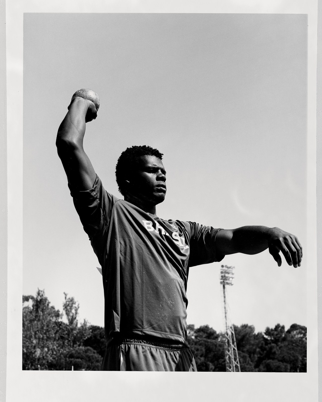 Brazilian shotputter with raised fist against clear sky at stadium.