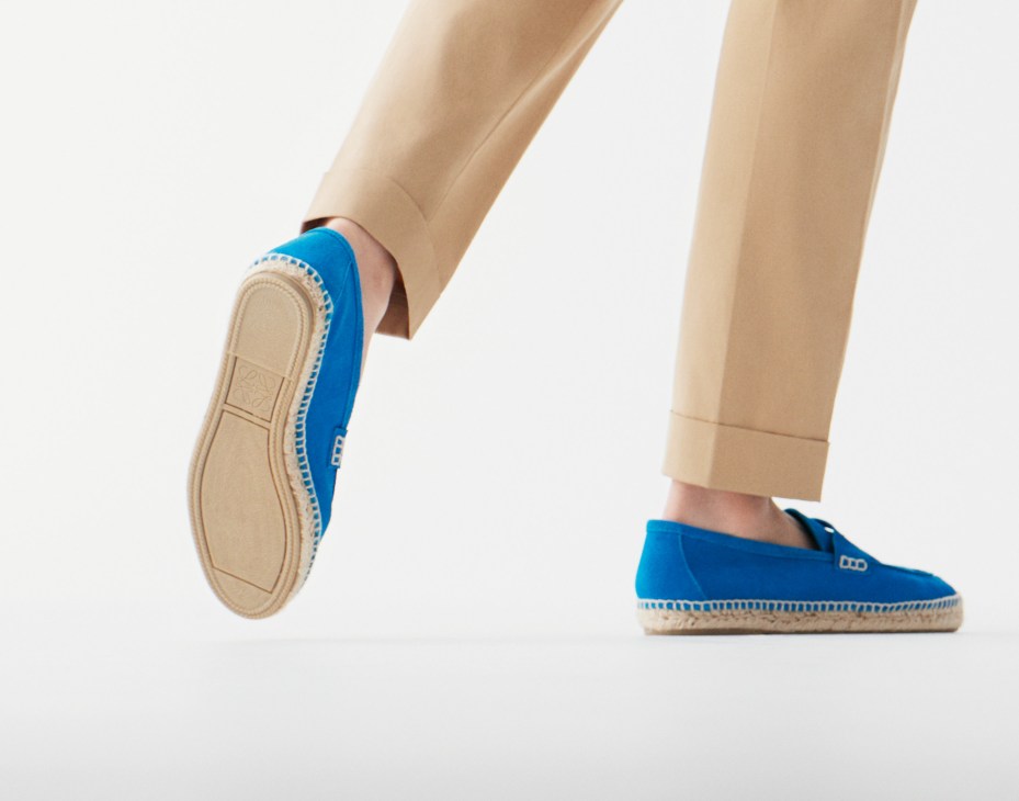 Person wearing beige trousers and blue slip-on espadrille shoes with cream soles.