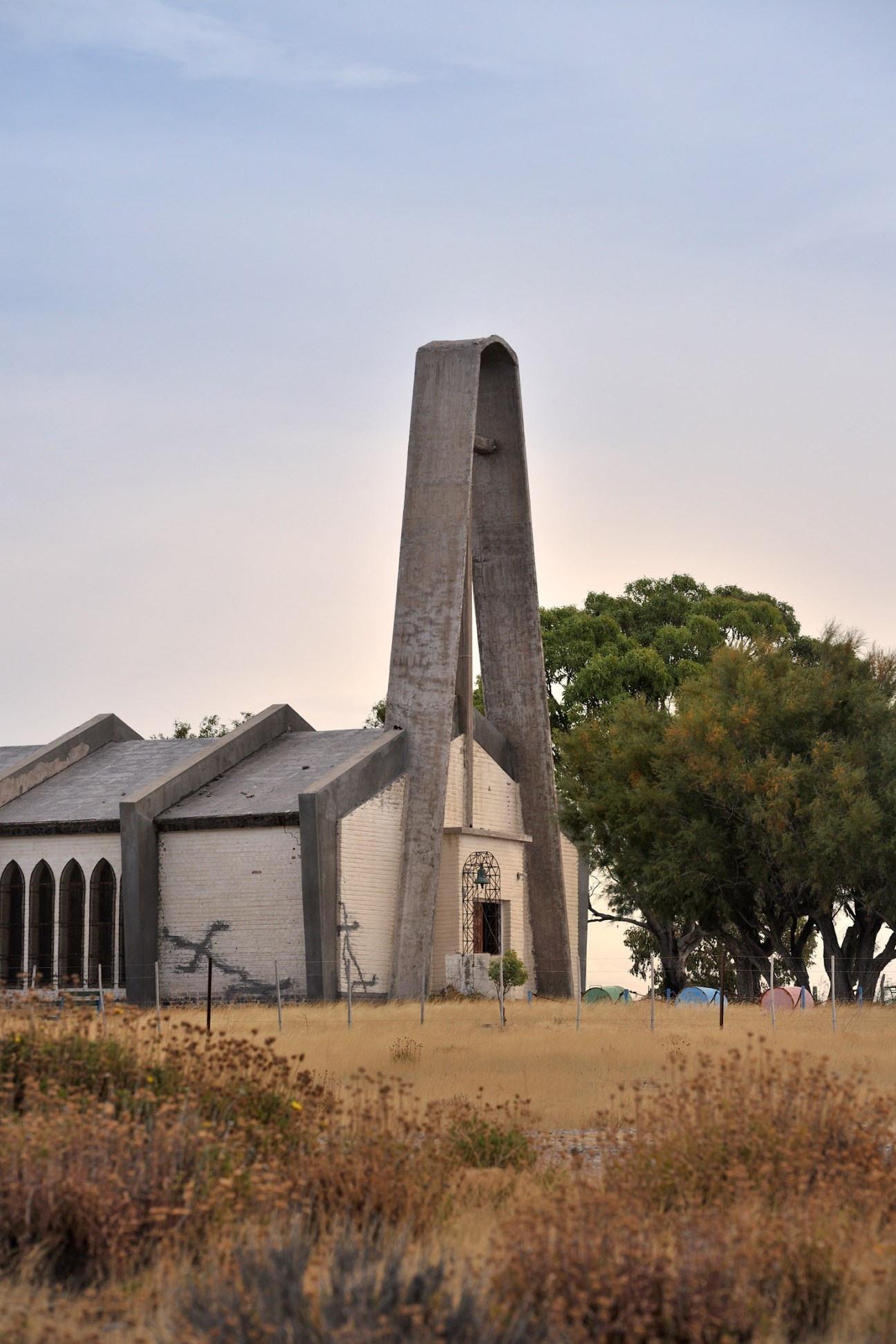 Modernist concrete church with tall angular tower standing in sparse Patagonian steppe landscape.