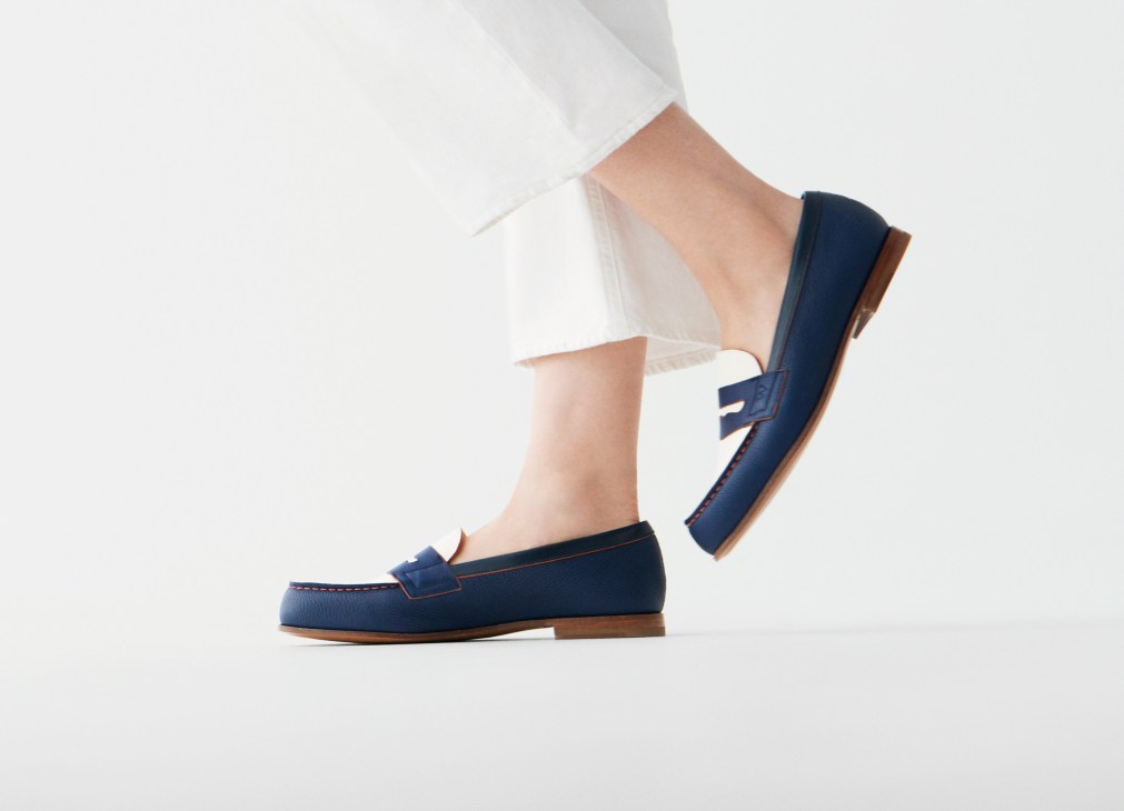 Model wearing white jeans and navy blue leather loafers with brown sole detail.