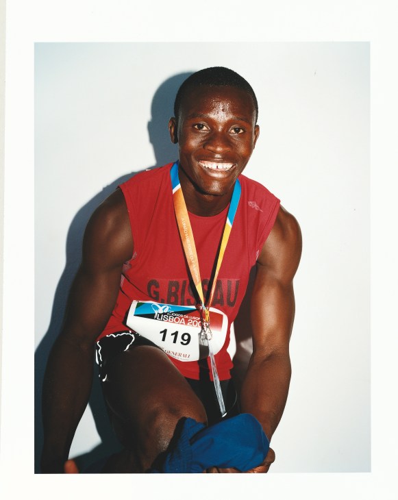 Male athlete from Guinea Bissau's 4x100m sprint team wearing red uniform and medal