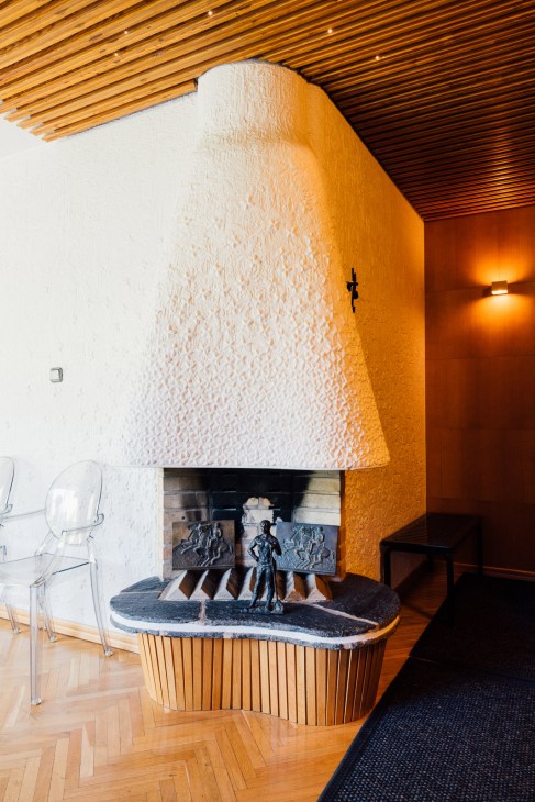 Modern corner fireplace with white textured wall, orange accent wall, wooden ceiling, and abstract bronze sculptures on dark hearth.