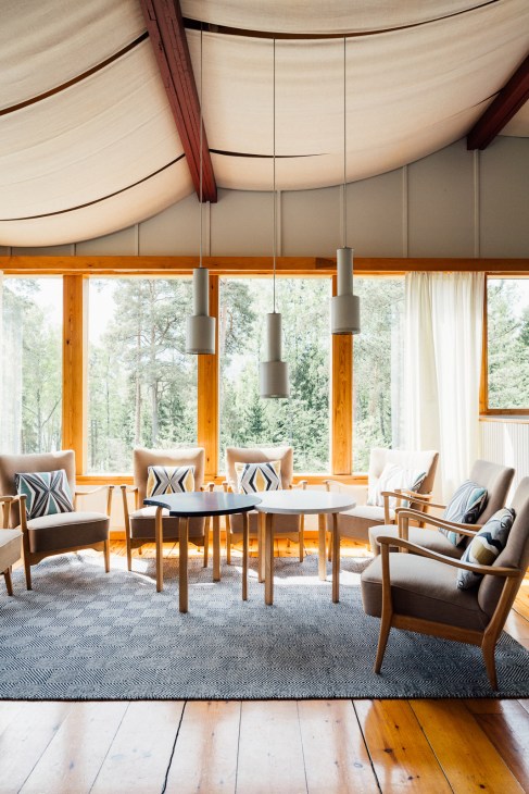 Modern interior with suspended pendant lights, wooden frames, mid-century chairs, and large windows overlooking forest at Kortvik Estate.