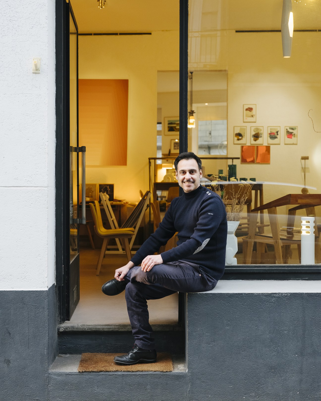 Man sitting in doorway of modern interior space with yellow walls and mid-century furniture