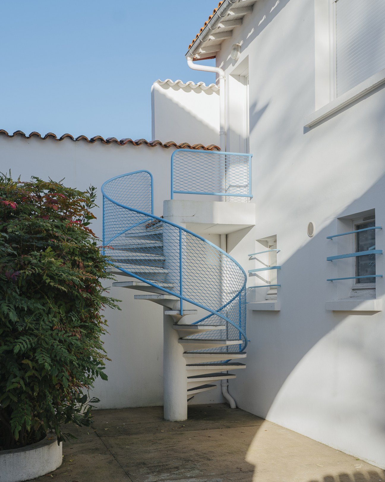 Blue spiral staircase with mesh railings on white modernist building exterior in Royan.