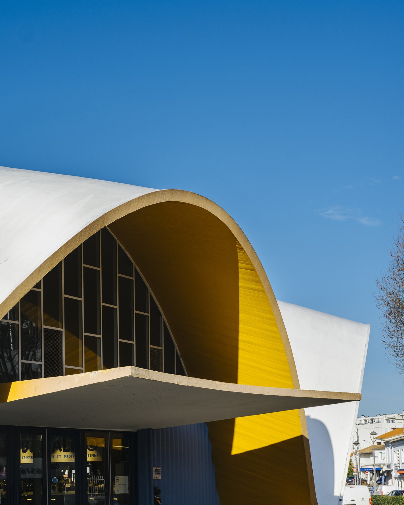 Royan's modernist market hall with white curved walls and bright yellow interior against a clear blue sky.