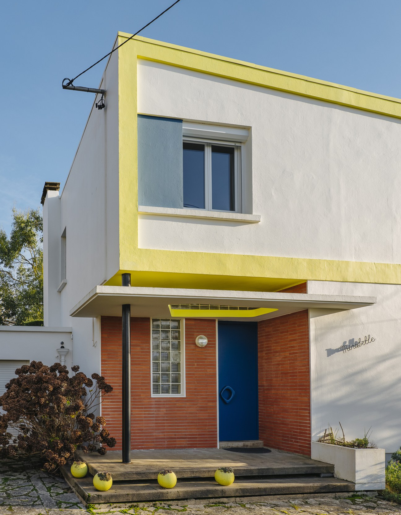 Villa Mirabelle, a modernist house in Royan with white walls, yellow trim, brick base, and bright yellow planters.