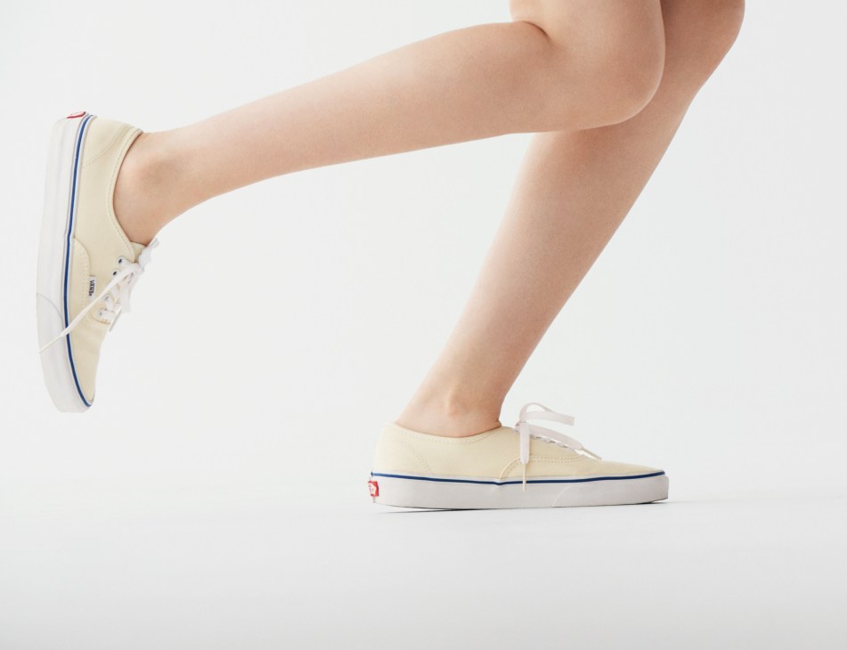 Person wearing cream-colored Vans sneakers with blue and red stripe details, shown from the legs down.