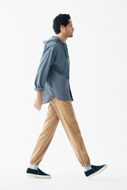 Man in profile walking wearing blue shirt, tan trousers, black and white trainers, and Muji socks.