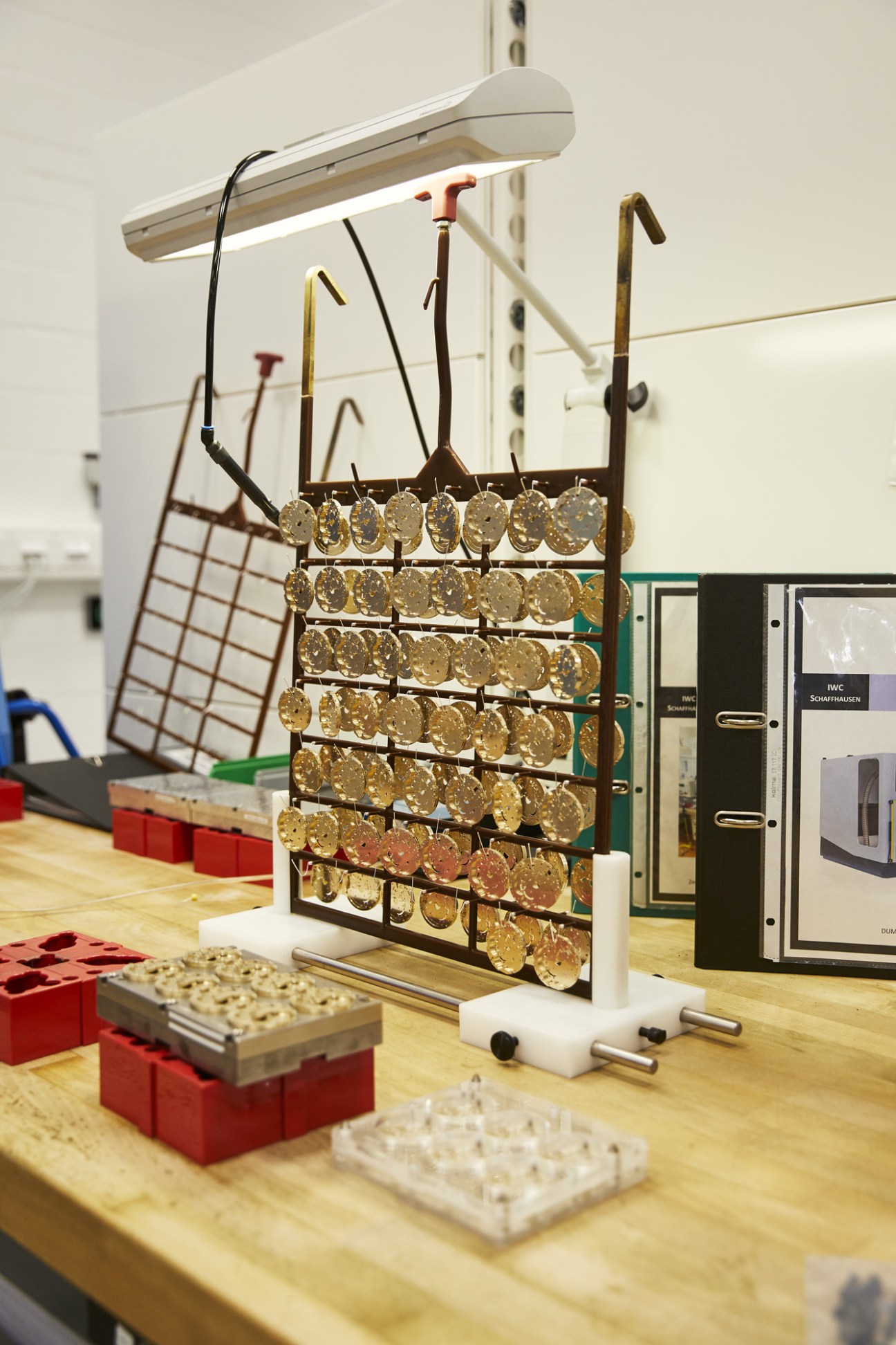 IWC watch parts and components organized on metal racks under laboratory lighting in production facility.