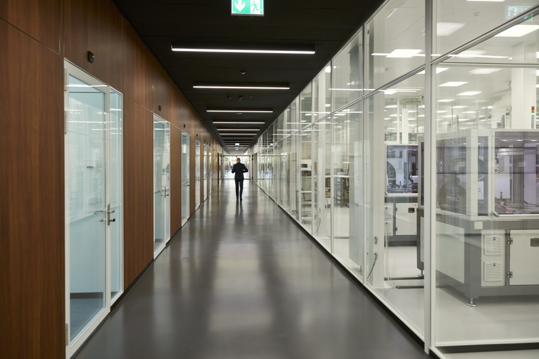 Modern corridor with glass-walled production rooms on right and wooden-paneled visitor area on left at IWC manufacturing facility.
