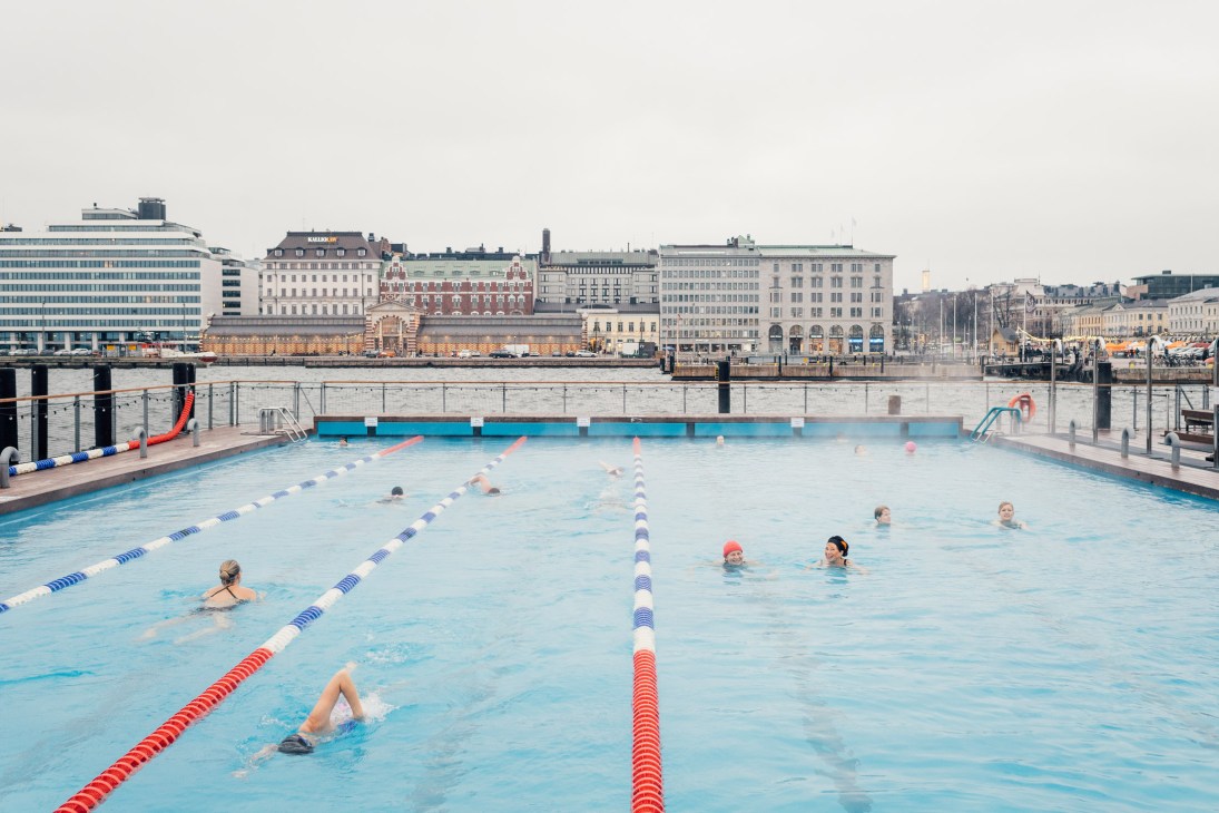 Swimmers in blue lanes at Allas Sea Pool in Helsinki with cityscape and harbor in background
