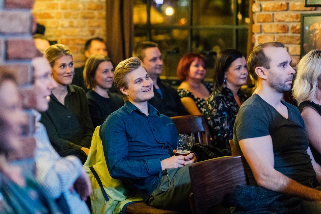 Group of people watching a performance at an indoor venue with exposed brick walls.