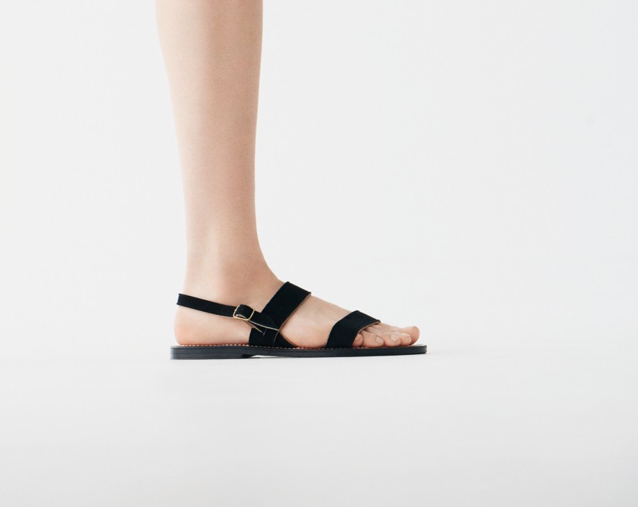 Black suede sandals with ankle straps and buckle details on a neutral background.