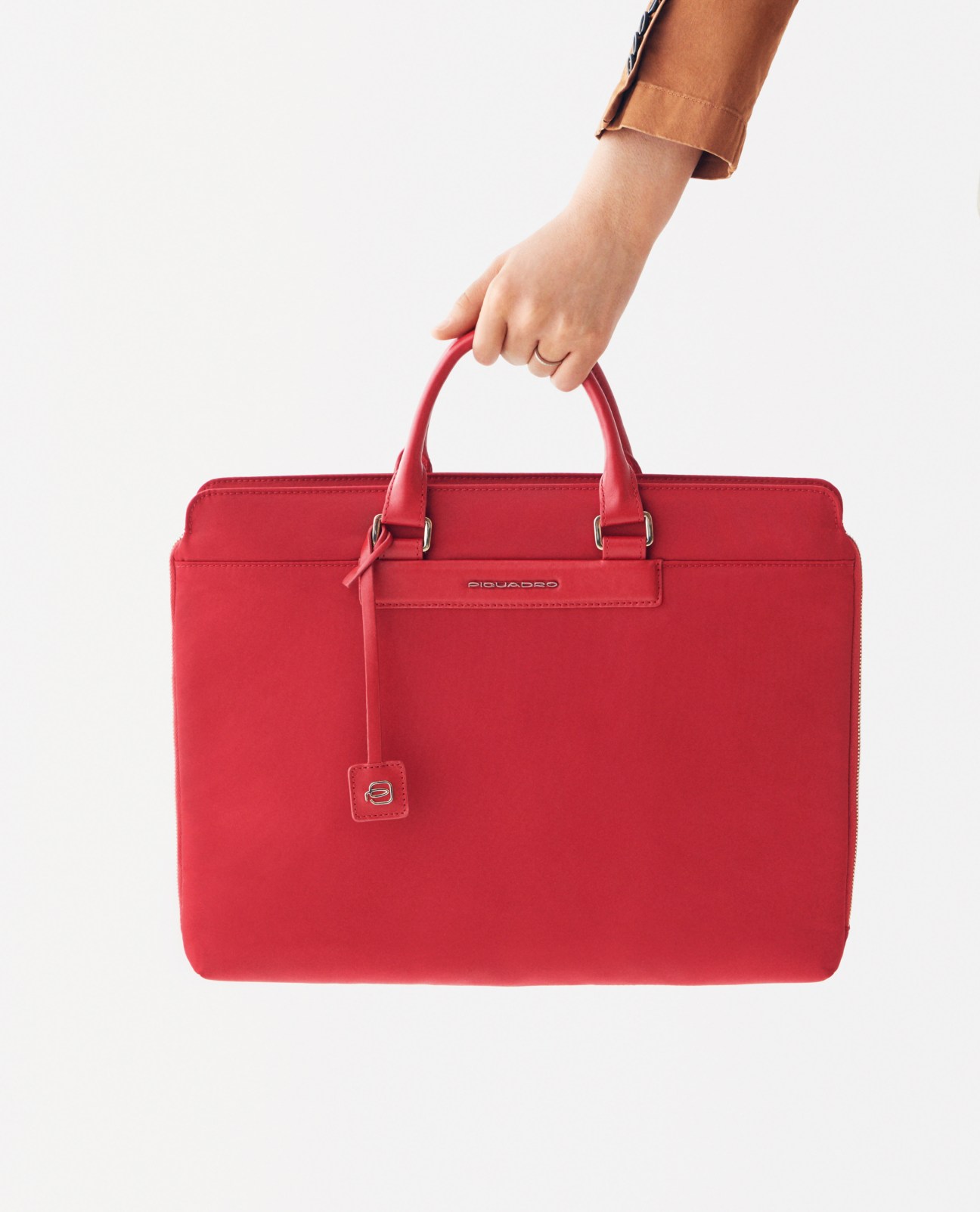 Hand holding a red Piquadro briefcase with leather handles against a white background.