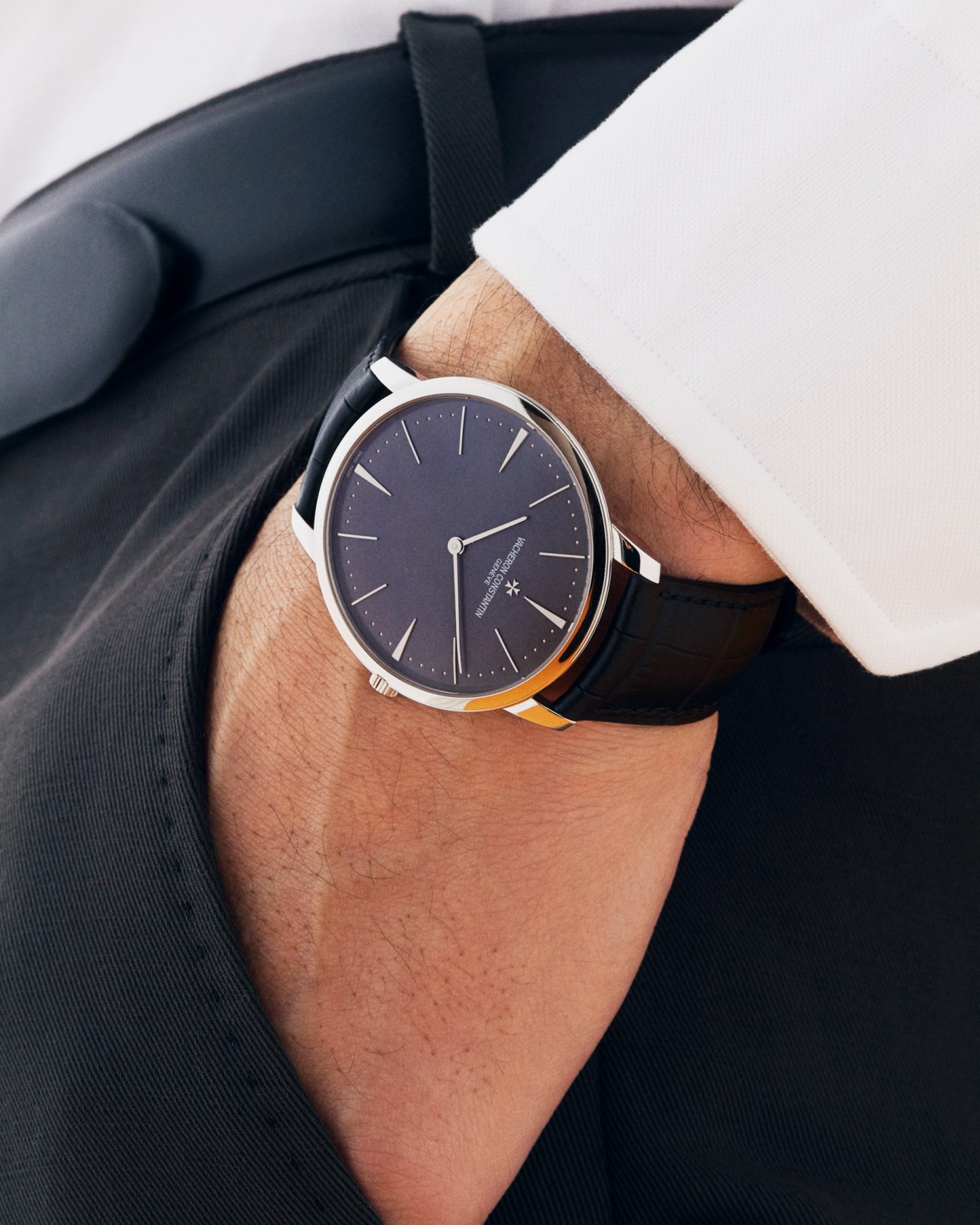 Vacheron Constantin watch with dark face and black leather strap worn on wrist above navy suit sleeve