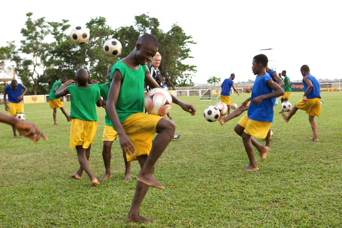Young football academy players in green and yellow uniforms practice on a grass pitch during a training exercise.