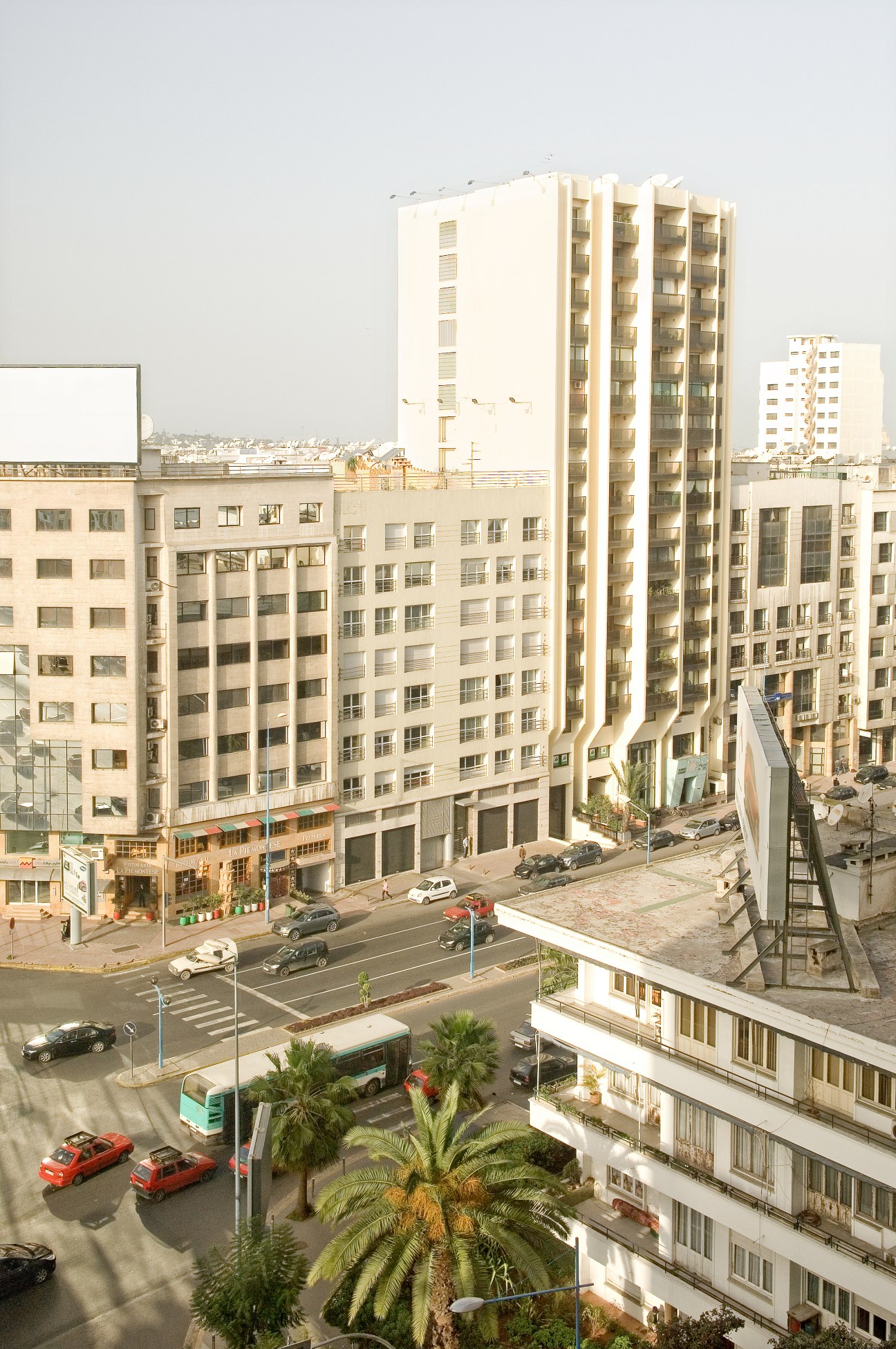 Urban street view of modern five-storey apartment buildings in Casablanca's Triangle d'Or neighbourhood with parked cars and palm trees.