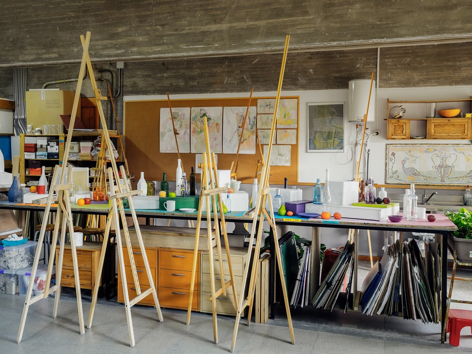 Art studio at Colegio Estudio with easels, paintbrushes, sketches on cork board, and shelves of supplies.