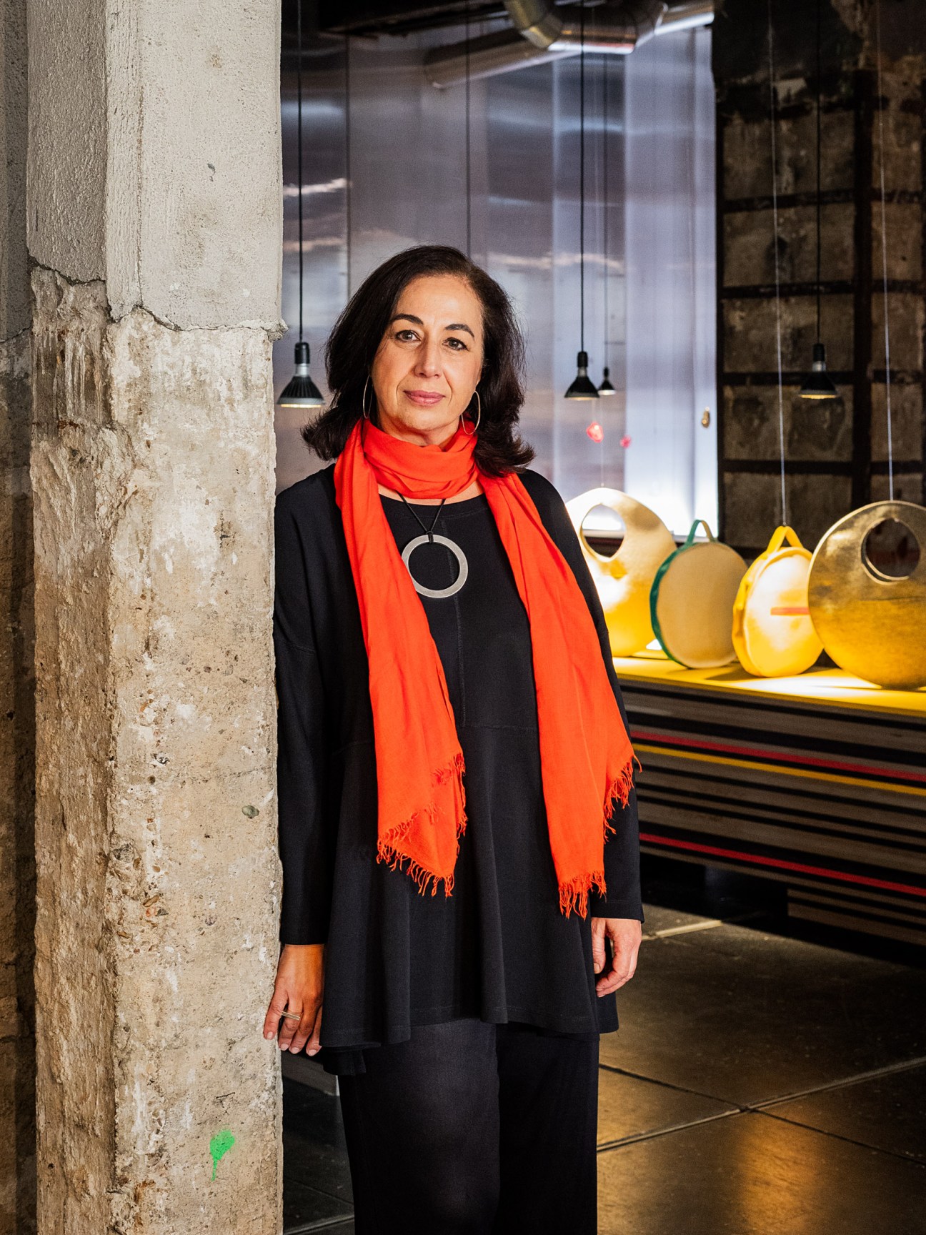 Graphic designer Miryam Anllo Vento stands in front of yellow sculptural vessels in a modern gallery space.
