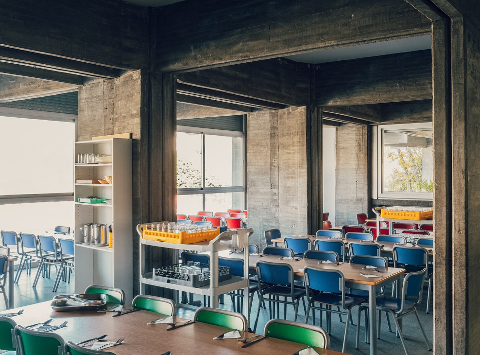 Dining area at Colegio Estudio with blue chairs, wooden tables, and brutalist concrete architecture.