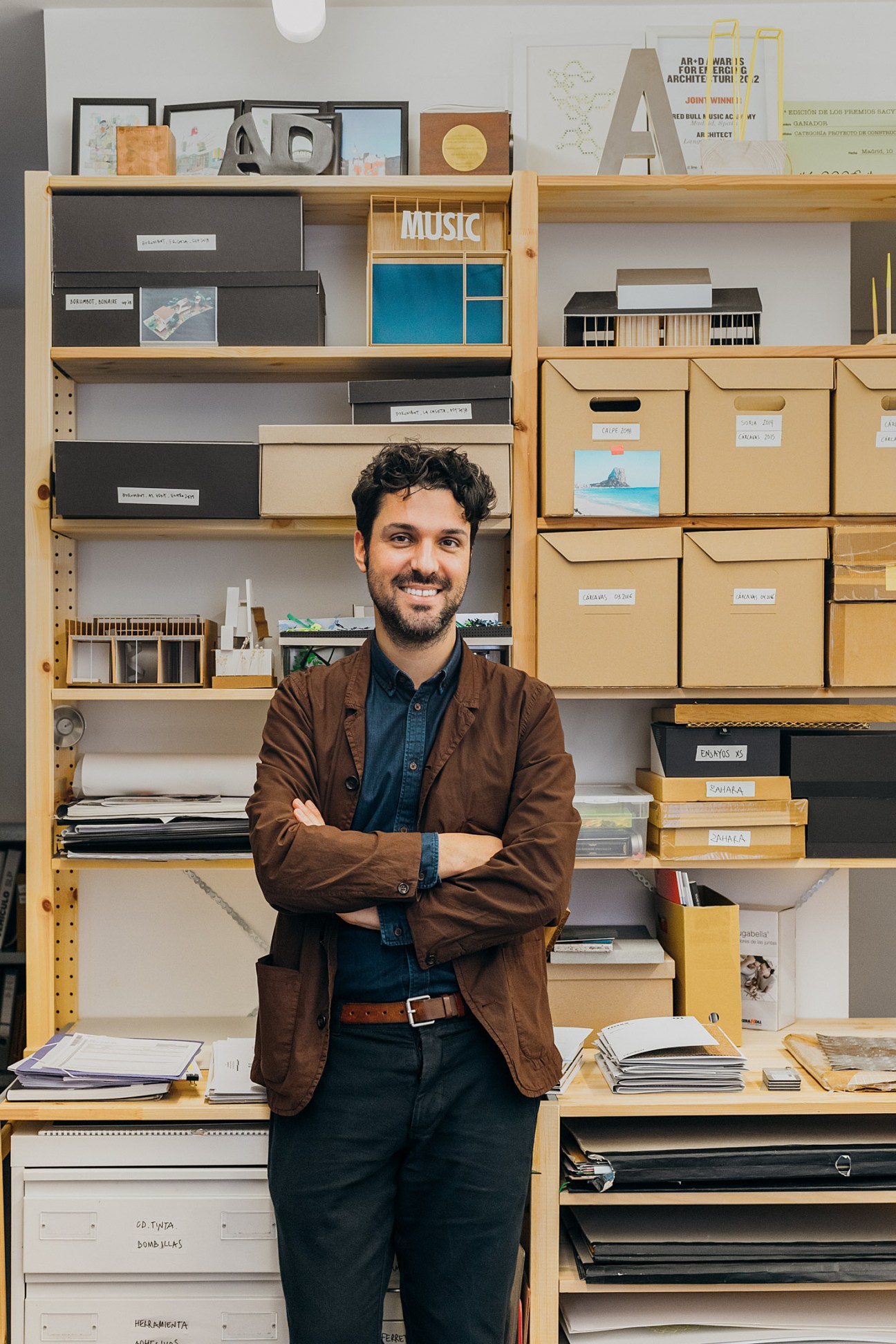 Architect Victor Navarro standing in front of wooden shelving displaying architectural models and design materials.