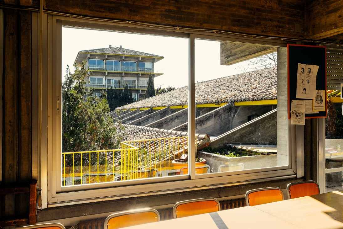View from a classroom through large windows showing Colegio Estudio's central tower and brutalist architecture with yellow railings.
