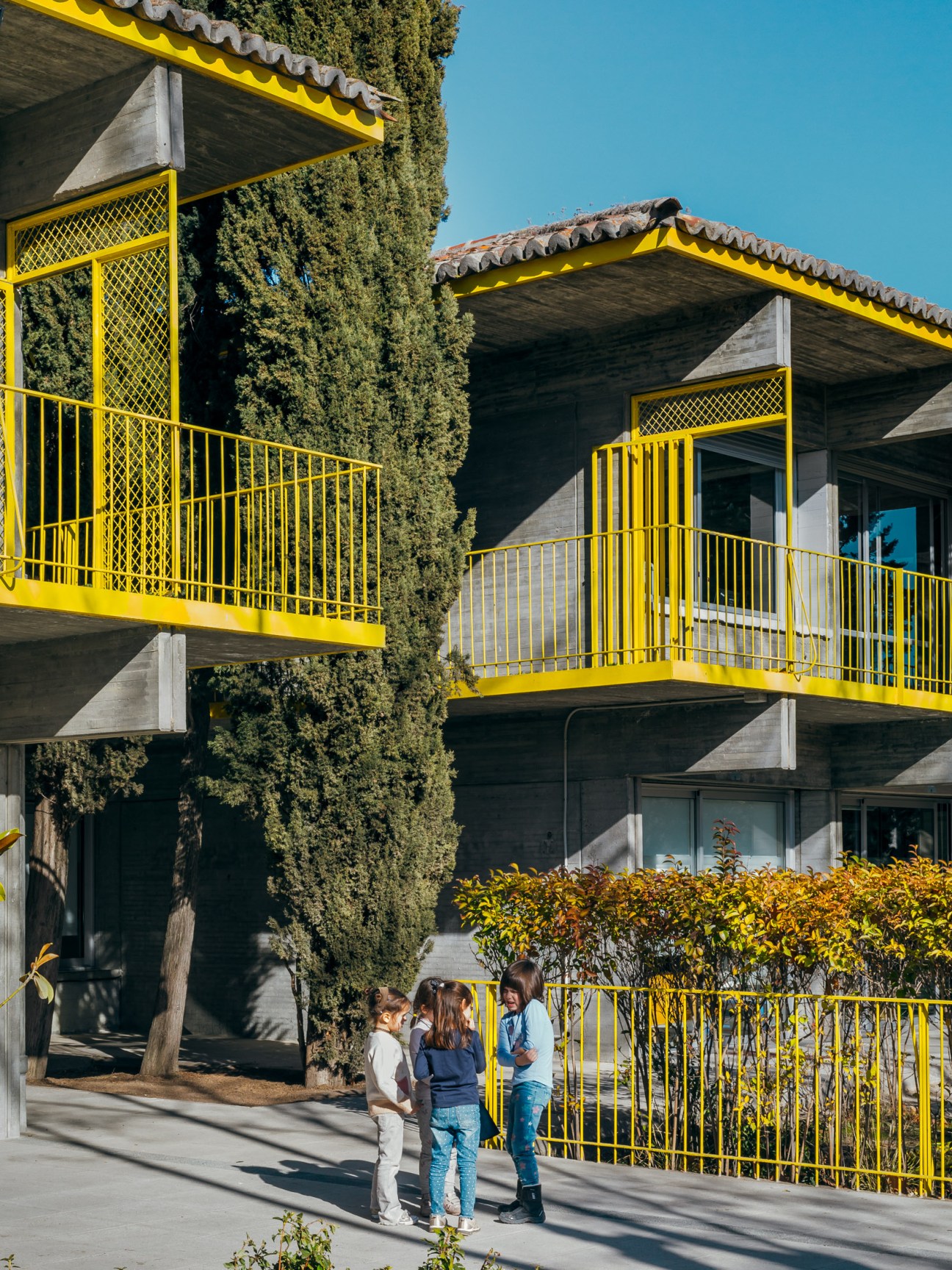 Students gathered outdoors at Colegio Estudio, with brutalist concrete architecture and bright yellow railings.