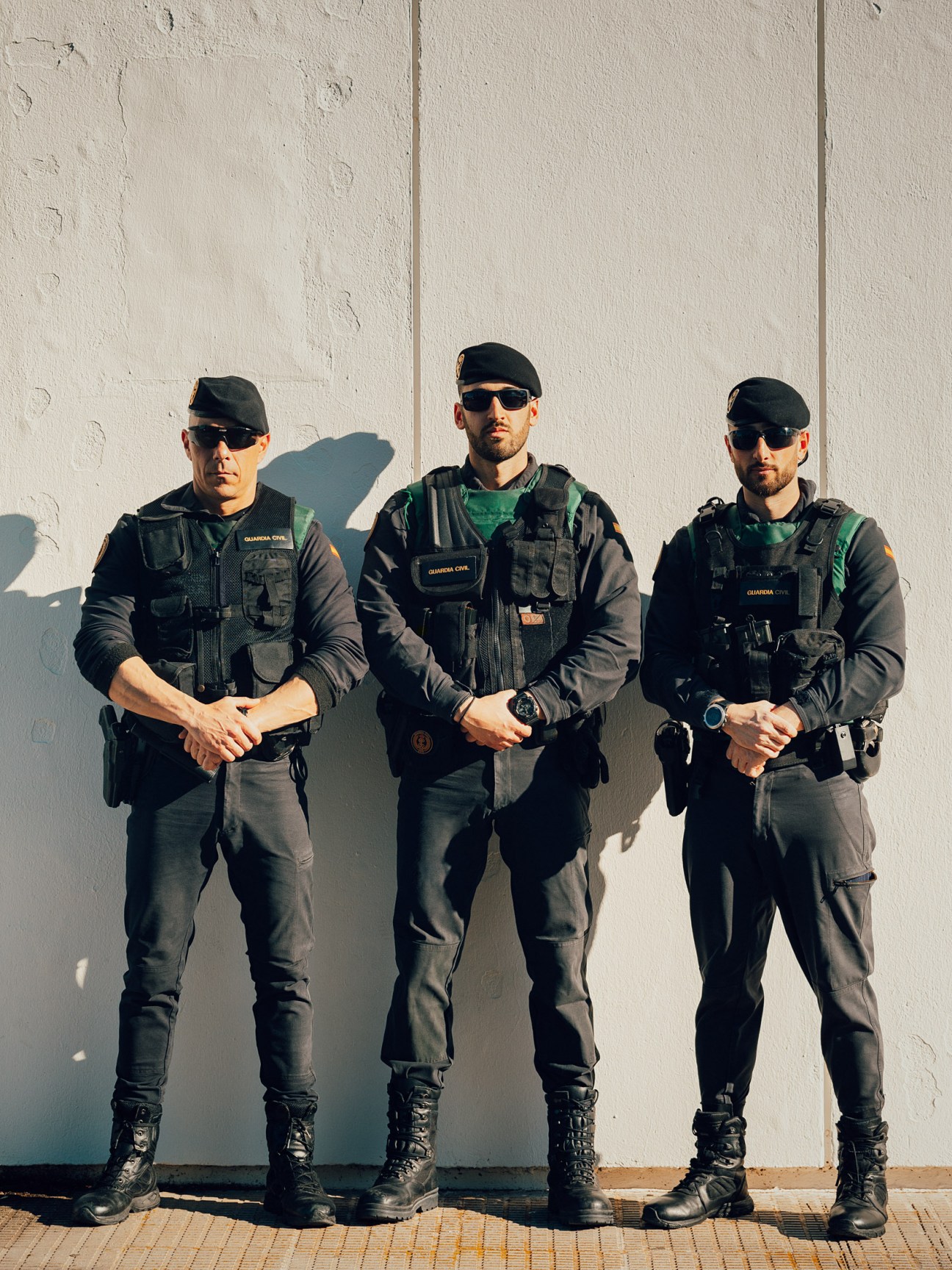 Three Guardia Civil agents in tactical gear stand against a white wall after a highway anti-narcotics operation.