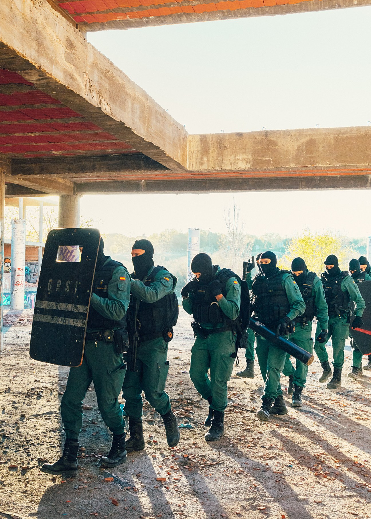 Guardia Civil GRS agents in green uniforms and face masks conduct a tactical training exercise under a concrete overpass.
